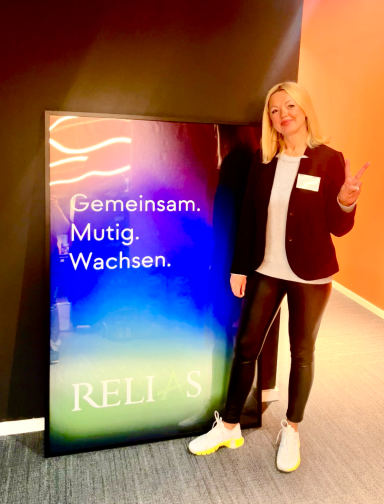 "Gemeinsam. Mutig. Wachsen." Olga Punko Frau steht neben einem großen Plakat mit dem Text "Gemeinsam. Mutig. Wachsen."